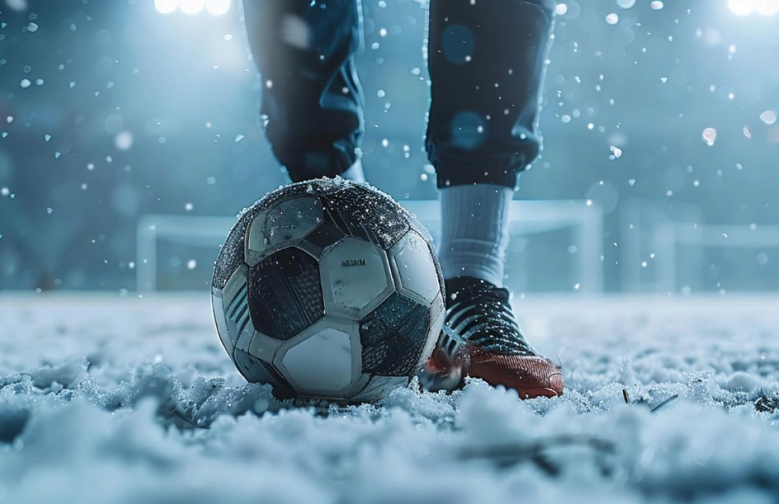 Soccer ball and player’s feet standing on a snowy, frozen pitch.