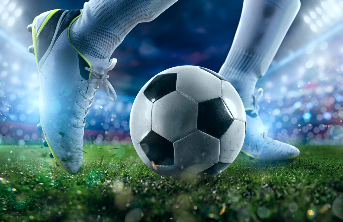 Football player taking a shot with a ball on a wet grassy field.